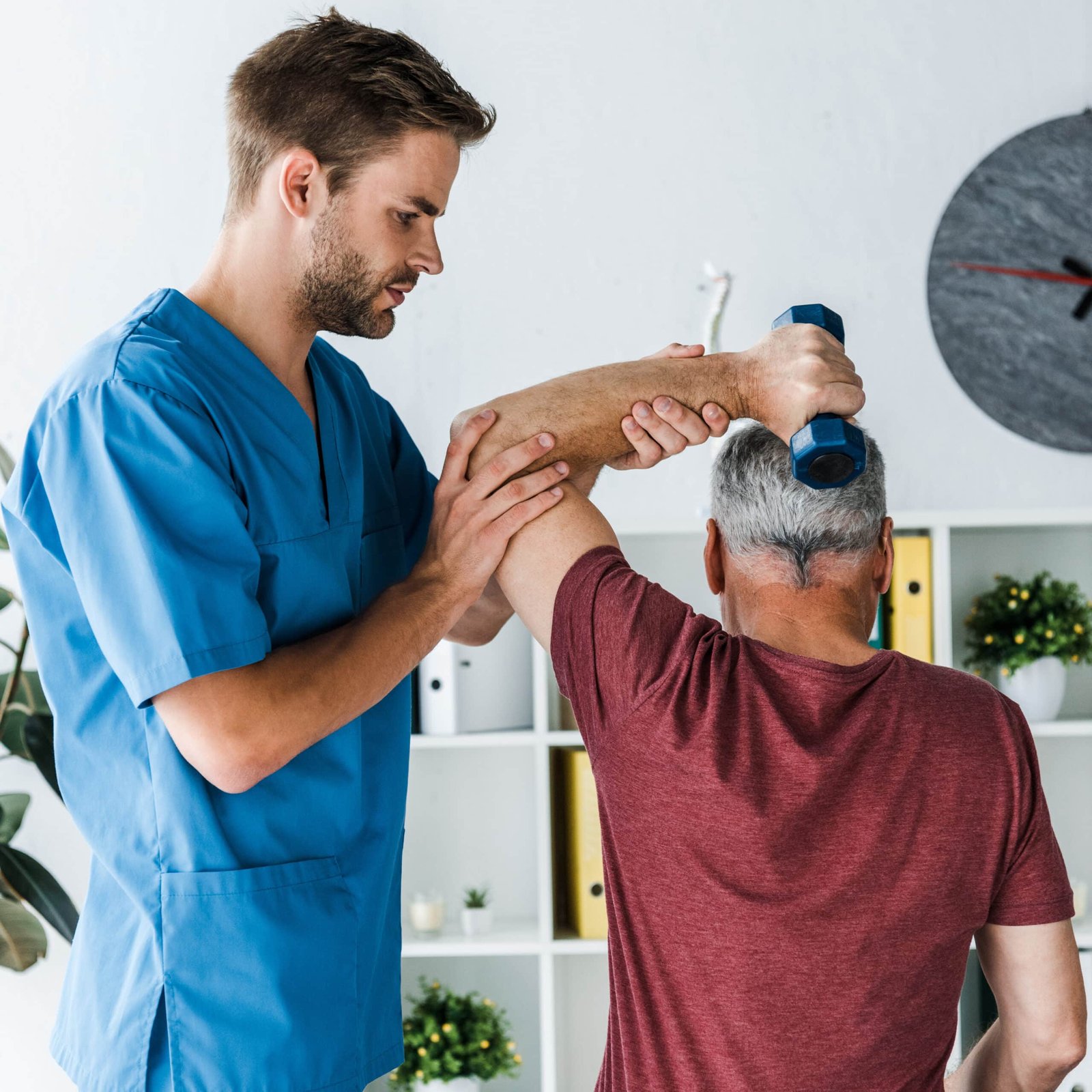 Back view of a middle aged man exercising with a dumbbell with a doctor